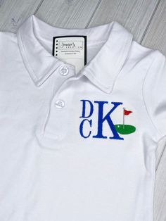 a white polo shirt with the letter k on it and a green, red, and blue flag