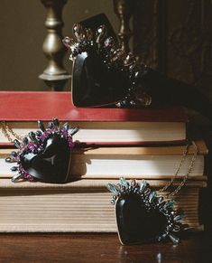 two black heart shaped pendants sitting on top of a stack of books next to each other