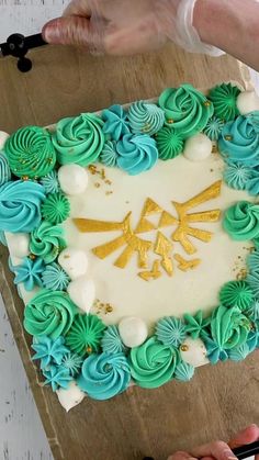 someone is cutting into a cake decorated with blue and green frosting on a wooden board