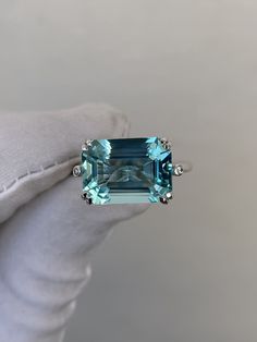 a ring with an aqua blue topazte surrounded by white diamonds on a gloved hand