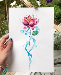 a person holding up a piece of paper with a watercolor painting of a flower on it