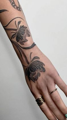 a woman's hand with black and grey tattoos on her left arm, holding onto the wrist