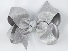 "Baby girls hair bow in metallic silver. 3\" size. Heat sealed dove-tail ends and a knotted center. Other colors shown on models for size reference. Stock up on this size grosgrain ribbon hair bows in over 90 colors in the shop 3\" Bundle Pack Each 3\" bow is made from 7/8\" wide grosgrain ribbon, and is securely mounted on a non-slip alligator clip to keep them perfectly in place. 1.75\" single prong alligator clip partially lined with matching ribbon Non-slip grip added to every bow High quali Metallic Silver Hair, Silver Hair Clips, Dove Tail, Girls Hair Bow, Silver Hair Clip, Bows Hair, Baby Hair Bows