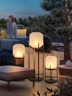 a woman standing on a deck next to two lamps and chairs with the lights turned on