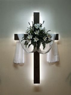 a cross with flowers on it in front of the light coming from behind curtaines