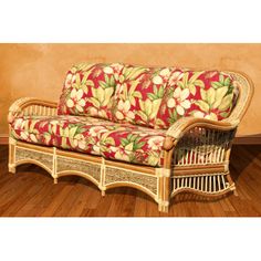 a wicker couch with red and yellow floral fabric on it, against a tan wall