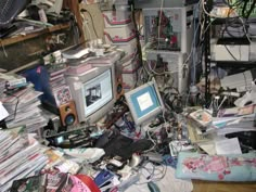 a cluttered room with many electronics and papers piled on top of eachother