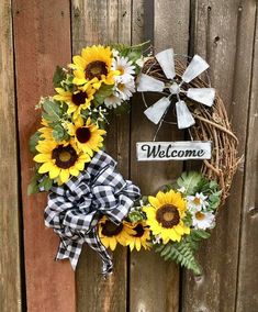 a wreath with sunflowers and a welcome sign on it hanging on a wooden fence