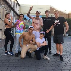 a group of young men and women posing for a photo on a brick sidewalk with one man wearing a tie dye shirt