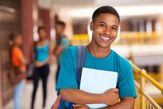 a young man is smiling and holding a folder in front of him while other people are walking down the hallway behind him