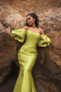 a woman in a yellow dress leaning against a rock