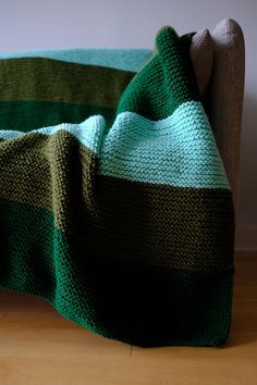 a green and brown blanket sitting on top of a couch next to a wooden floor