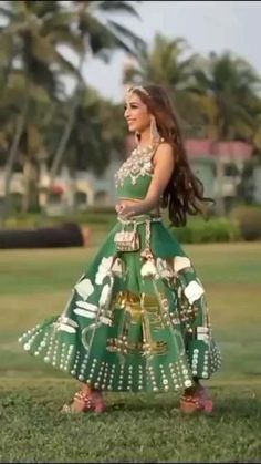 a woman in a green and gold dress is walking through the grass with palm trees behind her