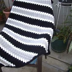 a black and white crocheted blanket sitting on top of a chair next to potted plants