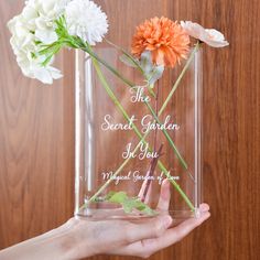 a person holding a vase with flowers in it that says the secret garden is you