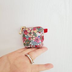 a hand holding a small purse on top of a white wall next to a finger