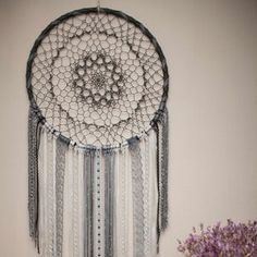 a white and gray dream catcher hanging on the wall next to a vase with purple flowers