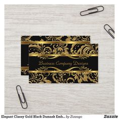 two business cards with black and gold designs on them, sitting next to some office supplies