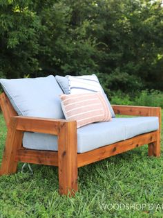 a wooden chair sitting in the grass with pillows on it's back and arms