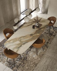 a marble dining table surrounded by brown chairs and an area rug in front of a large window