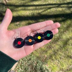 a person holding three small black earrings with colored circles on them in their palm,