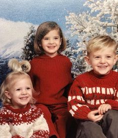 three young children sitting next to each other in front of a christmas tree with snow on the ground