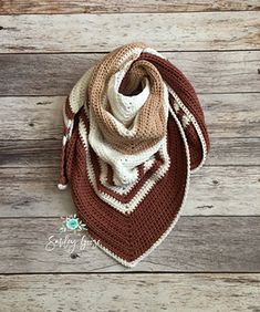 a brown and white crocheted scarf laying on top of a wooden floor