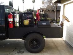 a black truck parked in front of a garage with tools on the bed and hoses attached to it