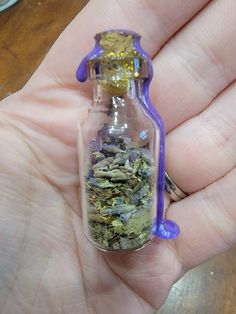 a hand holding a small glass bottle filled with tea and lavenders on it's side