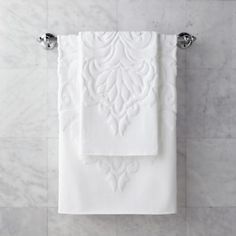 a white towel hanging on the wall next to two chrome faucets and a marble tiled floor