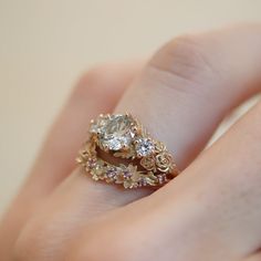 a woman's hand holding an engagement ring with flowers on the band and a diamond in the middle