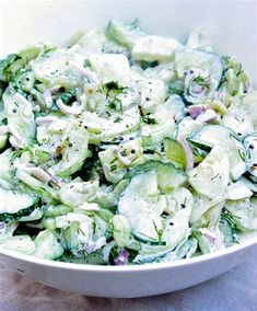 a white bowl filled with cucumber salad on top of a blue table cloth