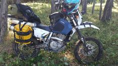 a blue and white motorcycle parked in the woods next to trees with backpacks on it