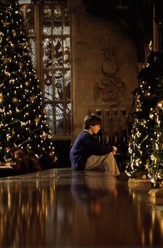 a woman sitting on the floor in front of christmas trees looking at her cell phone