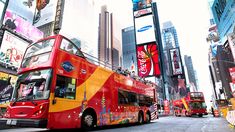 a red double decker bus driving down a street next to tall buildings and billboards