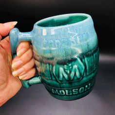 a hand holding a ceramic mug with writing on the outside and inside, in front of a black background