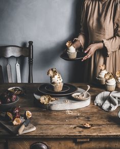 a woman holding a plate with cupcakes on it next to other desserts