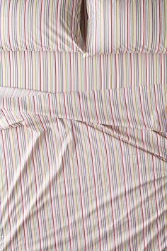 an unmade bed with red, yellow and blue striped sheets on it's side