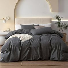 a bed with grey linens and pillows in a room next to a white toilet