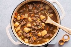 a pot filled with beef and potatoes on top of a table next to a wooden spoon