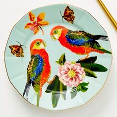 two colorful birds sitting on top of a plate with flowers and butterflies flying around them