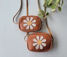 two brown purses with white flowers on the front and one has a tan strap