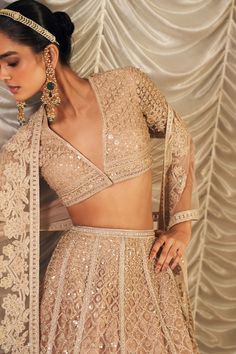 Exude opulence in the champagne net embroidered blouse, paired with a matching net embroidered lehenga and dupatta. The blouse features intricate embroidery in a soft champagne hue, offering a subtle yet luxurious sparkle. The lehenga, crafted from the same elegant net fabric, is richly embellished to complement the blouse. The net embroidered dupatta completes the look with its delicate, ethereal charm, making this ensemble perfect for any grand occasion. Glamorous Anarkali Set With Intricate Embroidery For Reception, Glamorous Lehenga With Intricate Embroidery For Reception, Glamorous Festive Choli With Intricate Embroidery, Glamorous Sets With Intricate Embroidery For Reception, Glamorous Designer Lehenga With Intricate Embroidery, Glamorous Wedding Sets With Resham Embroidery, Glamorous Festive Lehenga With Resham Embroidery, Festive Glamorous Lehenga With Resham Embroidery, Glamorous Lehenga With Unstitched Blouse For Designer Wear