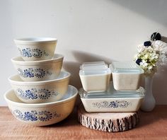 a stack of dishes sitting on top of a wooden table next to a vase with flowers