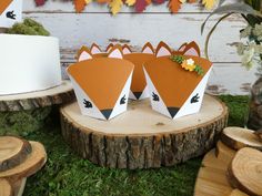 two paper foxes sitting on top of a tree stump in front of a cake and flowers