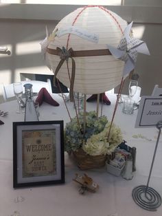 a hot air balloon is sitting on a table with flowers and decorations around it, next to a framed sign that says welcome