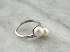 This sweet pearl ring has a classic bypass style design setting these pearls side by side. Easy to wear day or night, this vintage ring is a classic and timeless wardrobe staple! Metal: 14K White Gold Gem: 2 Pearls Gem Measurements: 7 mm, Round Ring Size: 6 Marks: "KSK 14K" Stamped on the inside band Luxury Classic Pearl Ring With Prong Setting, Pearl Cocktail Ring, Ring Pearl, Vintage Cocktail Ring, Timeless Wardrobe, Bypass Ring, Timeless Wardrobe Staples, Vintage Cocktail, Round Rings