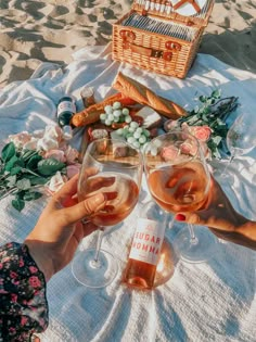 two people toasting wine glasses on the beach with food and drinks in front of them