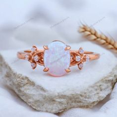 an opal and diamond ring sitting on top of a rock next to some wheat