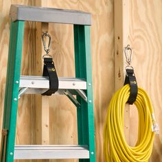 a yellow hose connected to a green stepladder next to a wooden wall and ladder